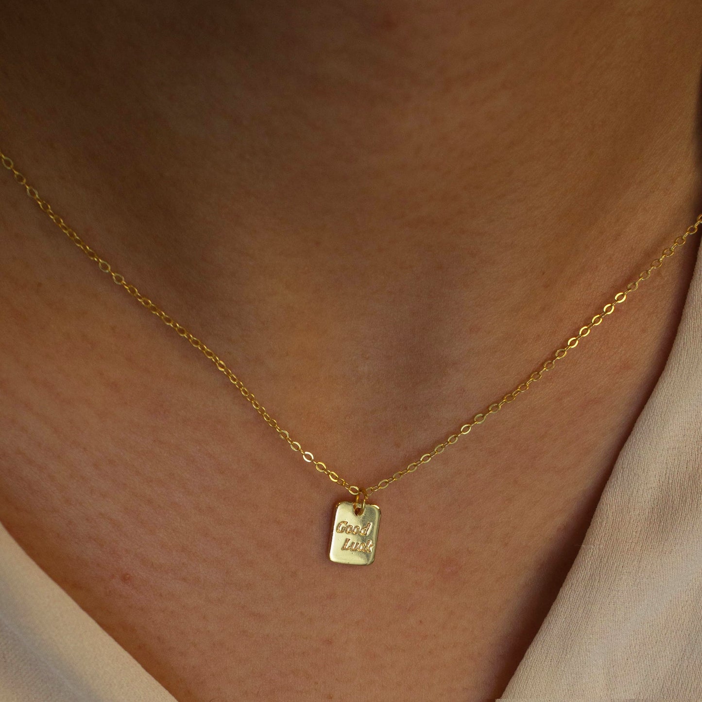 This photo features a thin chain necklace made of 14K gold-plated sterling silver, paired with a tag pendant with the words 'good luck'.