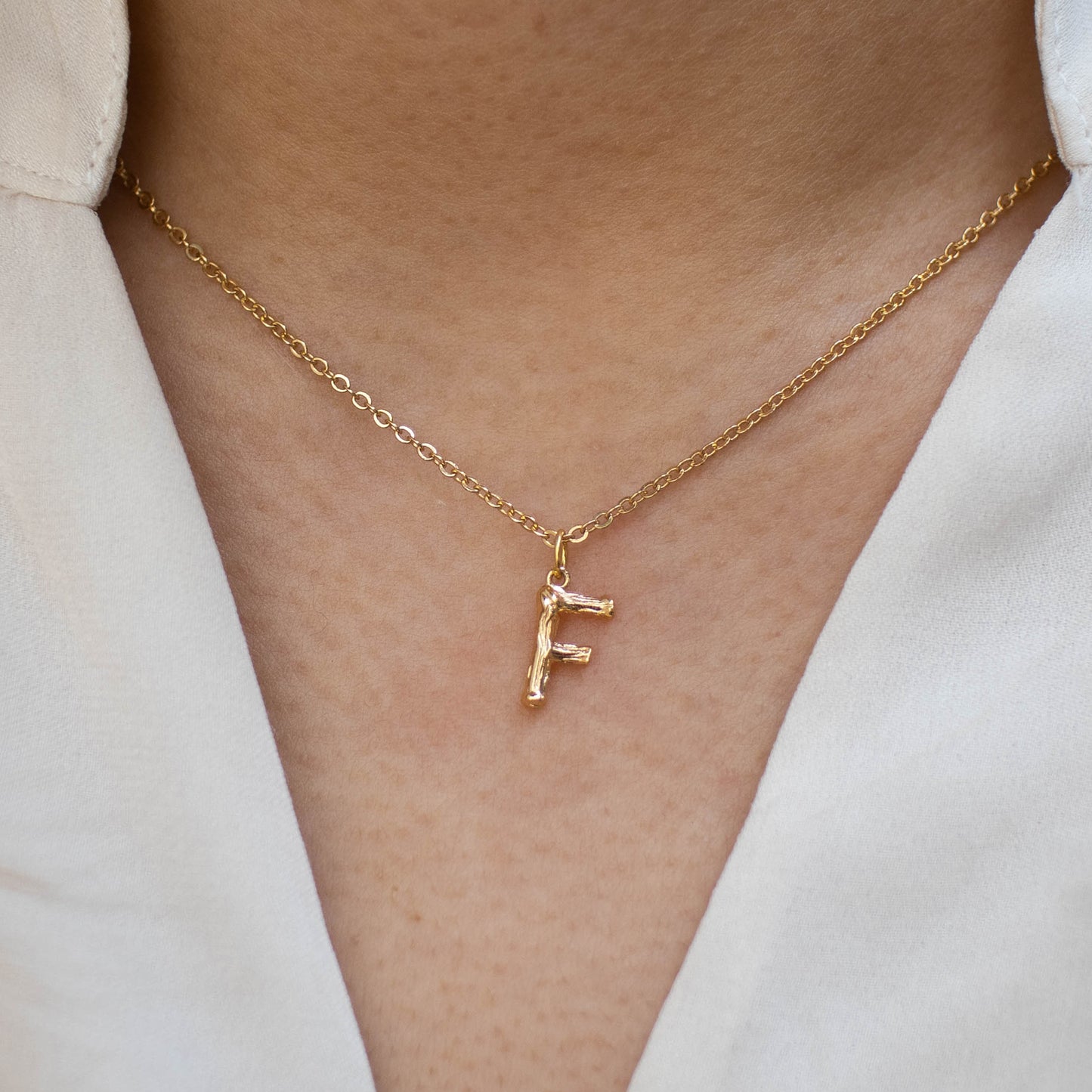 This photo features a thin chain necklace made of 14K gold-plated sterling silver, paired with a golden Letter pendant.