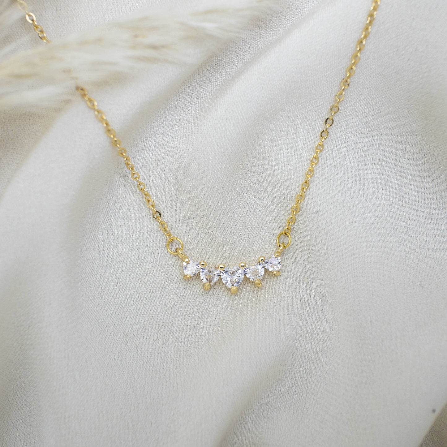 This photo features a thin chain necklace made of 14K gold-plated sterling silver, paired with a rectangular tag pendant with Five Zircon Heart Necklace