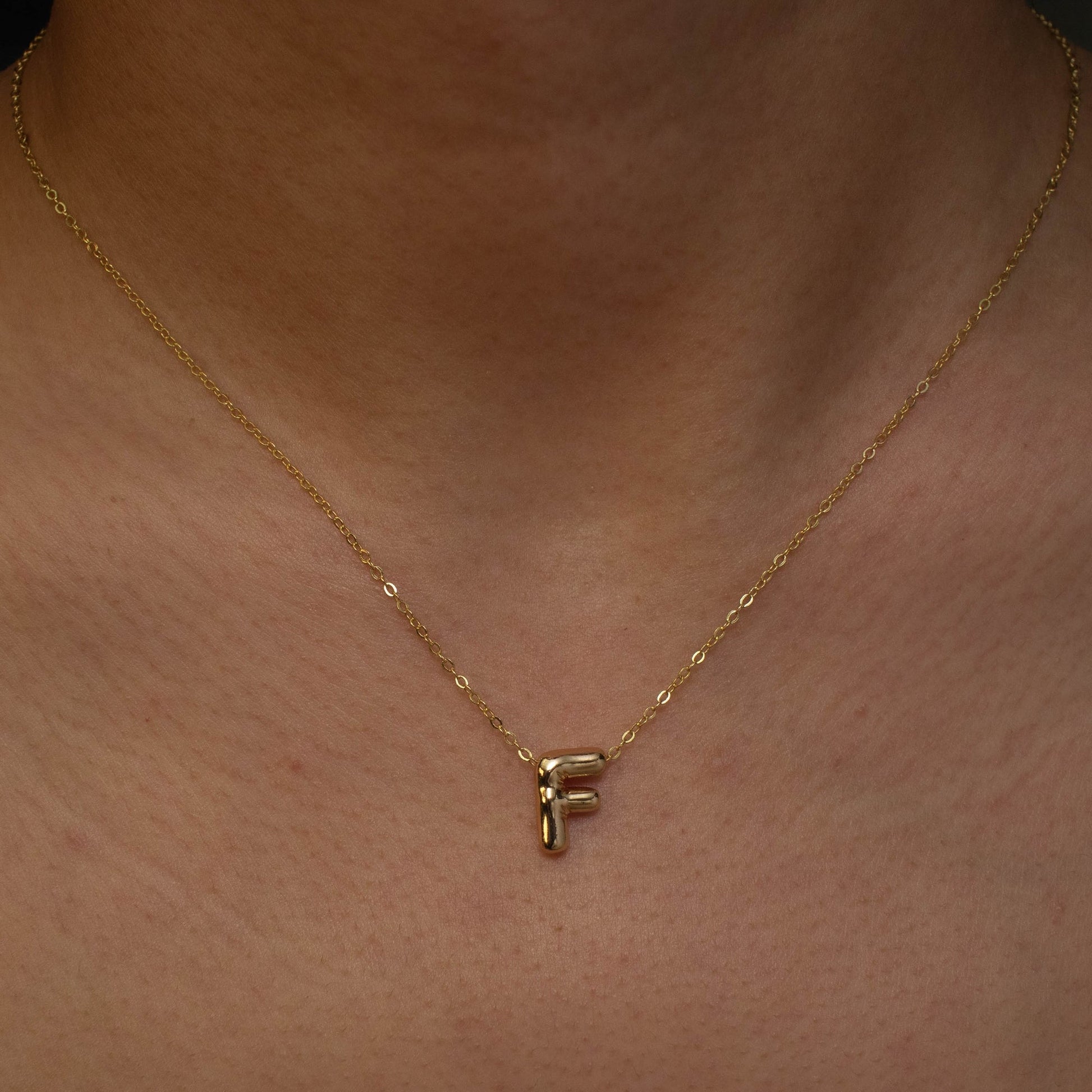 This photo features a thin chain necklace made of 14K gold-plated sterling silver, paired with a golden Bubble Letter pendant.