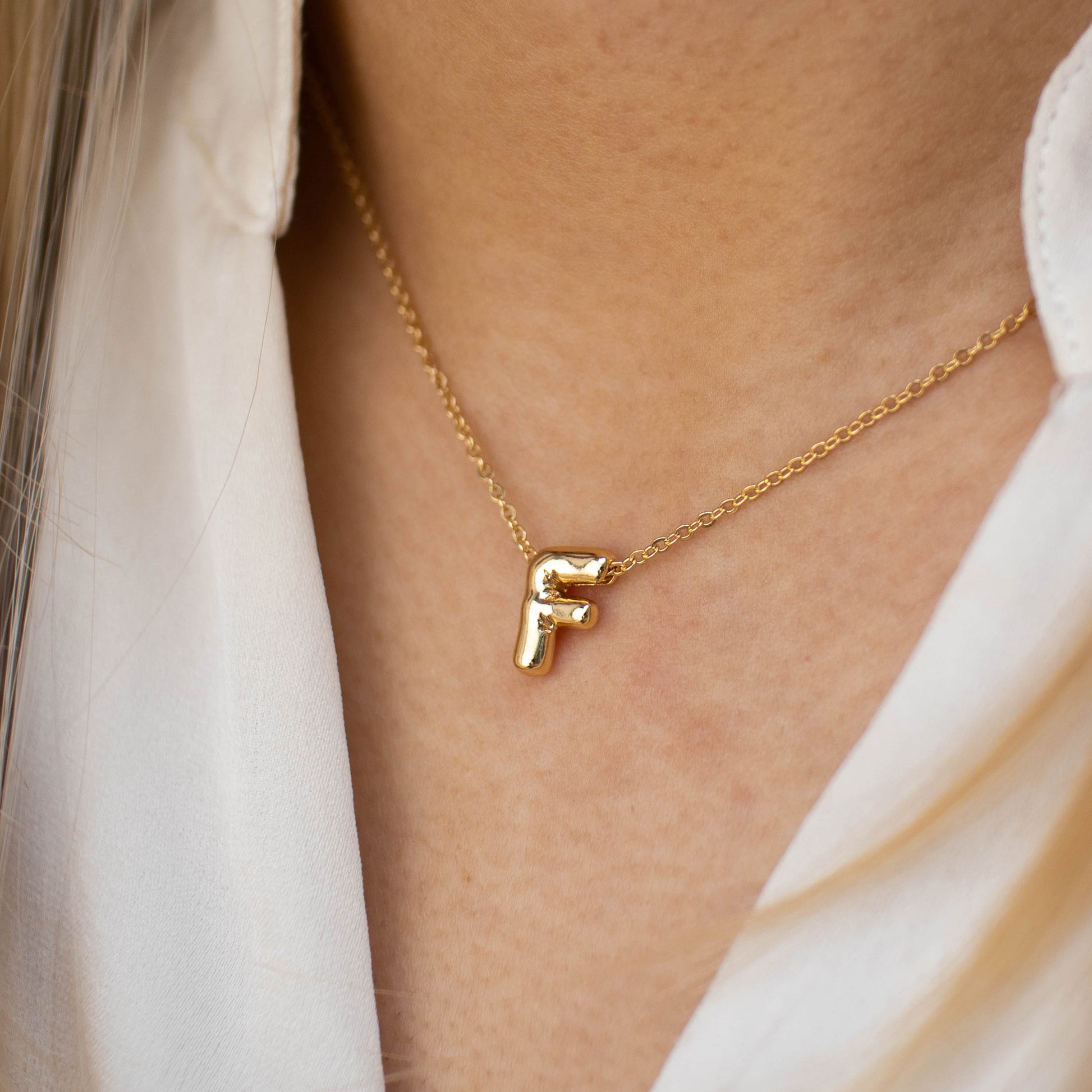 This photo features a thin chain necklace made of 14K gold-plated sterling silver, paired with a golden Bubble Letter pendant.