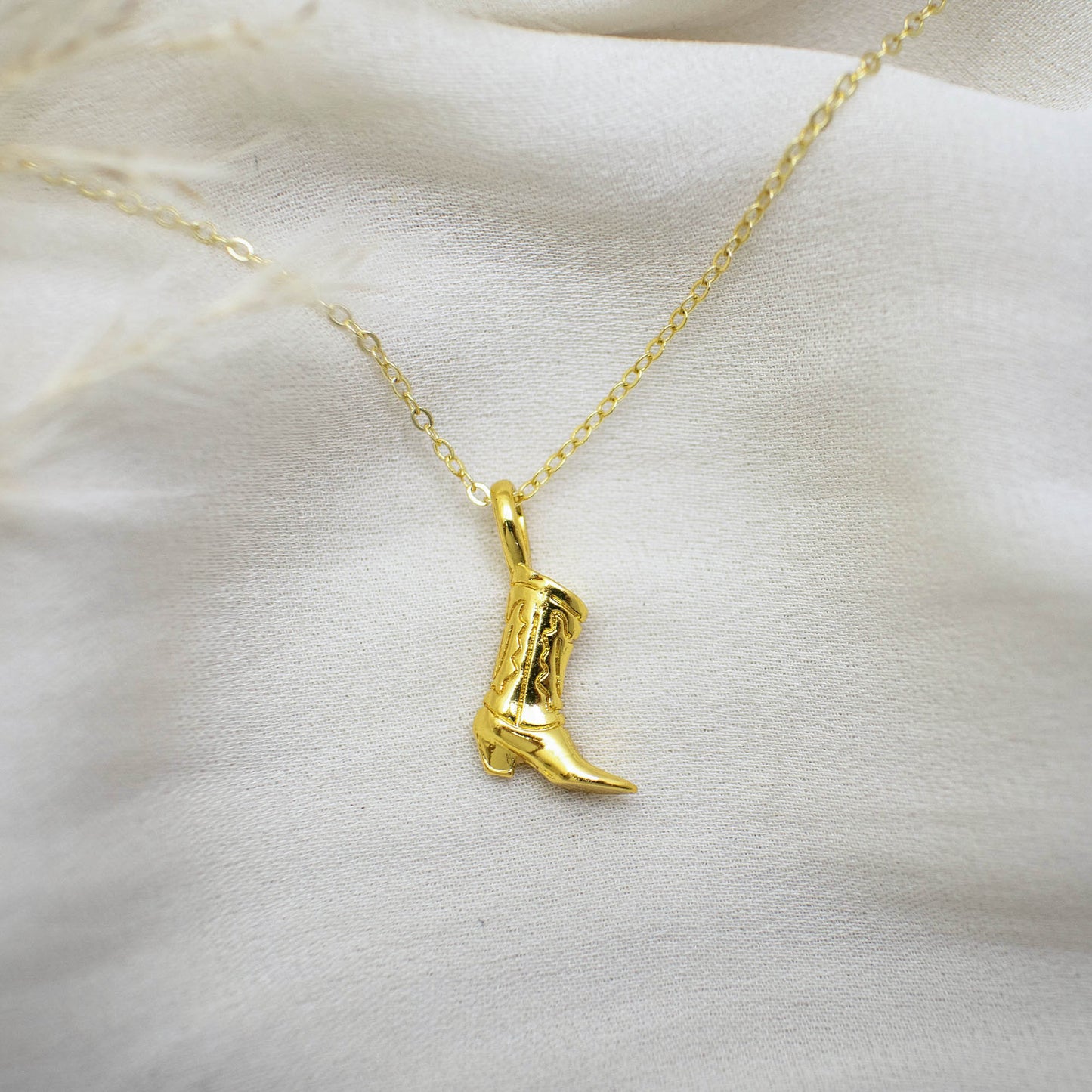 This photo features a thin chain necklace made of 14K gold-plated sterling silver, paired with a cute cowboy boot pendant.