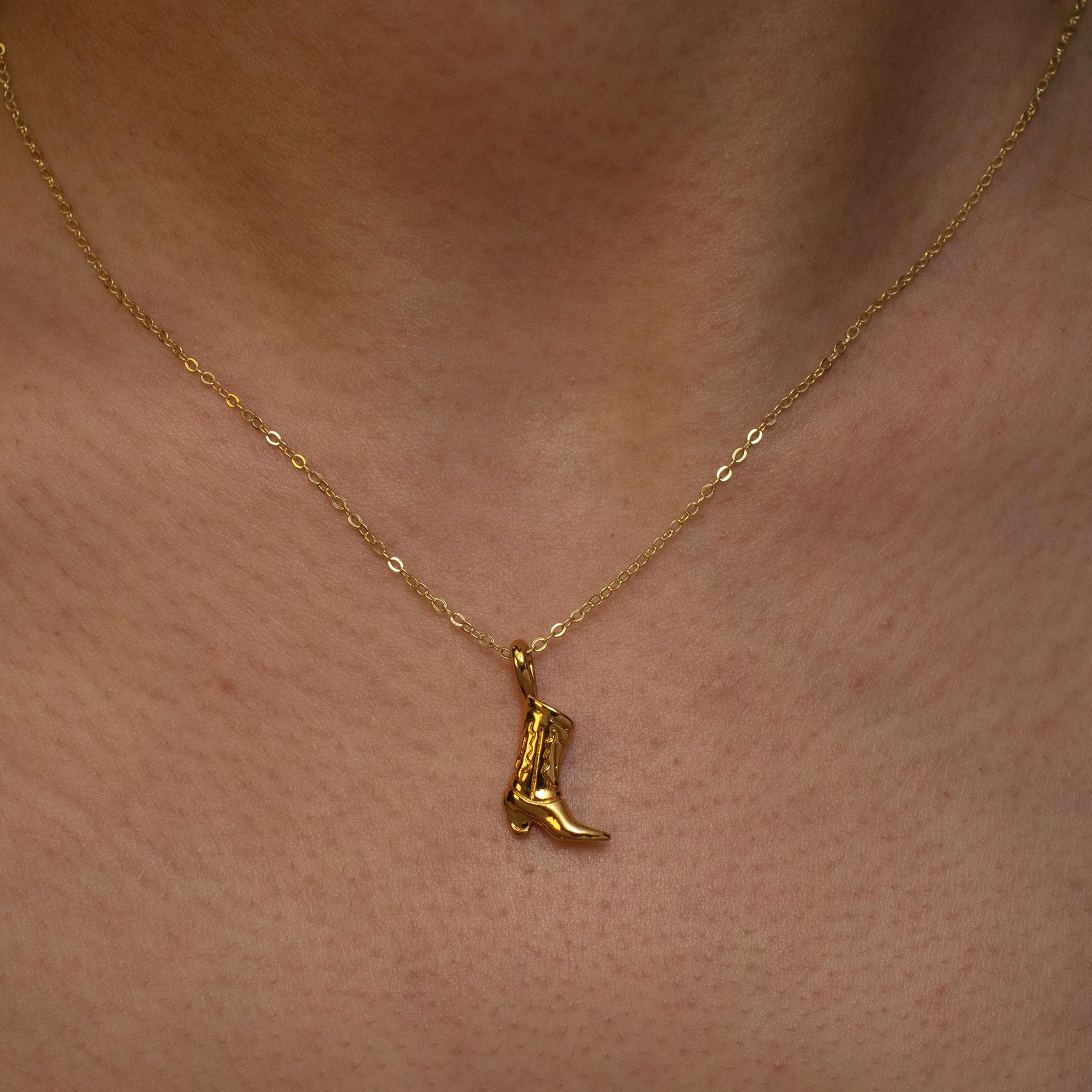 This photo features a thin chain necklace made of 14K gold-plated sterling silver, paired with a cute cowboy boot pendant. It's a sophisticated, elegant, and minimalist jewelry.