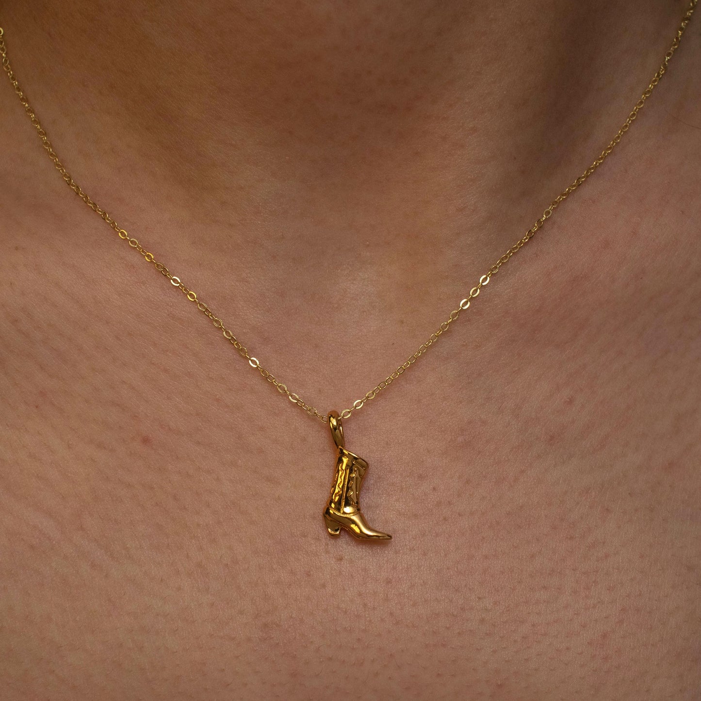 This photo features a thin chain necklace made of 14K gold-plated sterling silver, paired with a golden cowboy boot pendant.